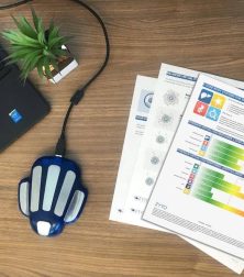 Laptop on desk with health reports, a blue device, and a small plant for a modern and organized workspace setup.