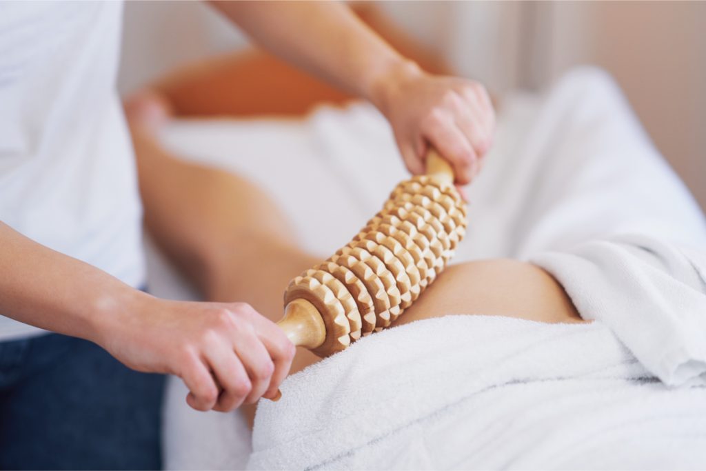 Person receiving a relaxing manual wood therapy massage with a textured roller on a towel-covered leg.