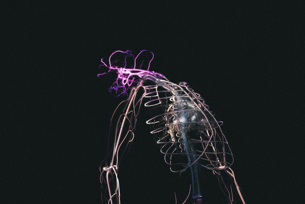 Abstract sculpture with glowing purple wires against black background, creating a modern art installation.