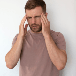 Man with a headache holding temples, eyes closed in pain against a white background.
