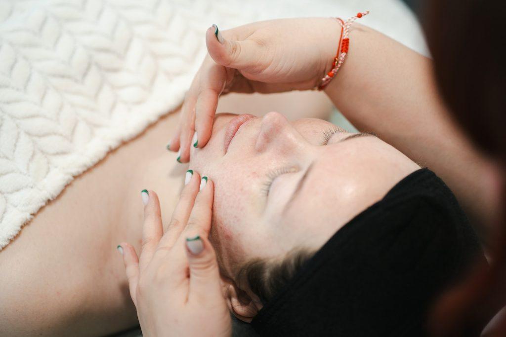 Person receiving a relaxing facial massage at spa, covered with a soft towel, promoting wellness.