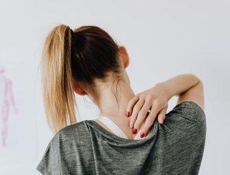 Woman in gray shirt holding her neck, indicating neck pain or tension.